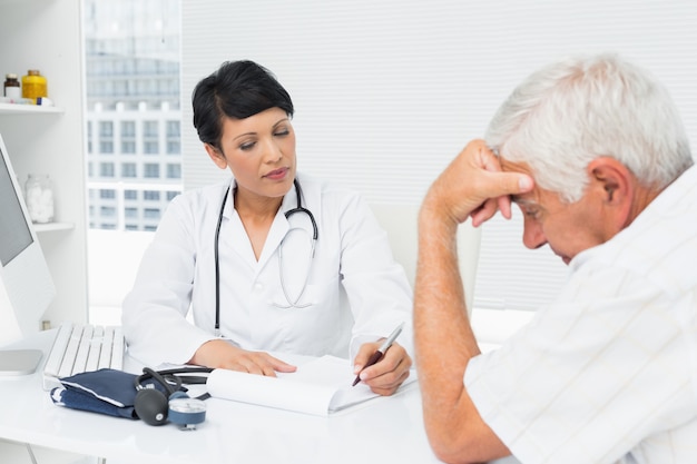 女性の医者は、医療事務所で心配している高齢者の患者に報告を説明する