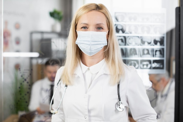 Female doctor in face mask and lab coat posing indoors