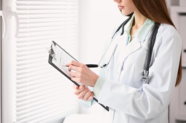 Female doctor filling up medical history standing near the window in hospital