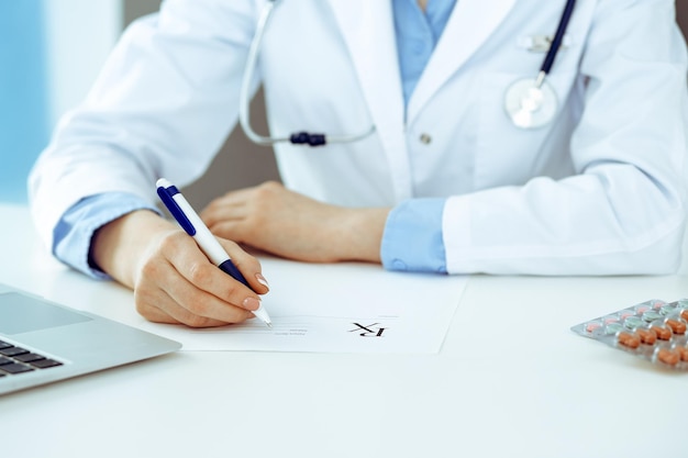 Female doctor filling up prescription form while sitting at the desk in hospital closeup.  Healthcare, insurance and excellent service in medicine concept