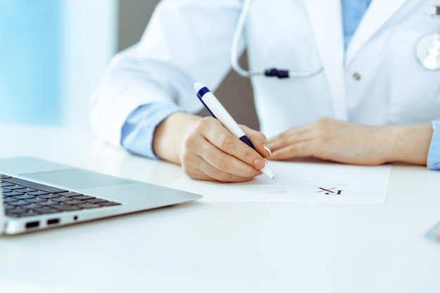 Female doctor filling up prescription form while sitting at the desk in hospital closeup Healthcare insurance and excellent service in medicine concept