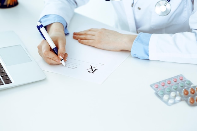 Female doctor filling up prescription form while sitting at the desk in hospital closeup Healthcare insurance and excellent service in medicine concept