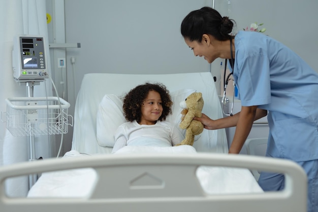 Photo female doctor giving teddy bear to child patient in the ward