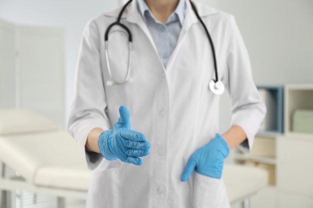 Female doctor in gloves offering handshake indoors closeup