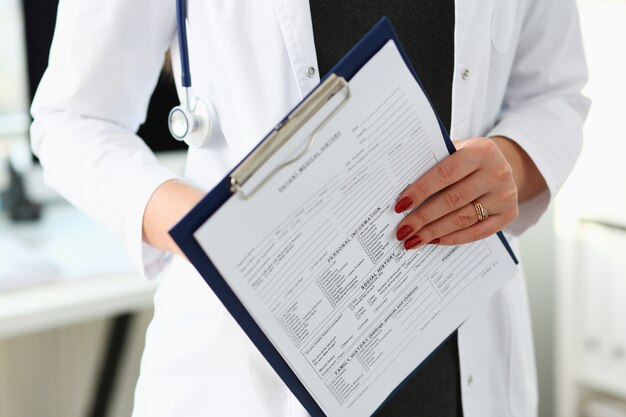 Female doctor hand holding and filling patient history list at clipboard pad during physical. Exam er disease prevention ward round visit check 911 prescribe remedy healthy lifestyle concept.