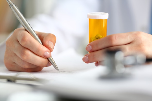 Female doctor hand holding jar of pills and writing prescription