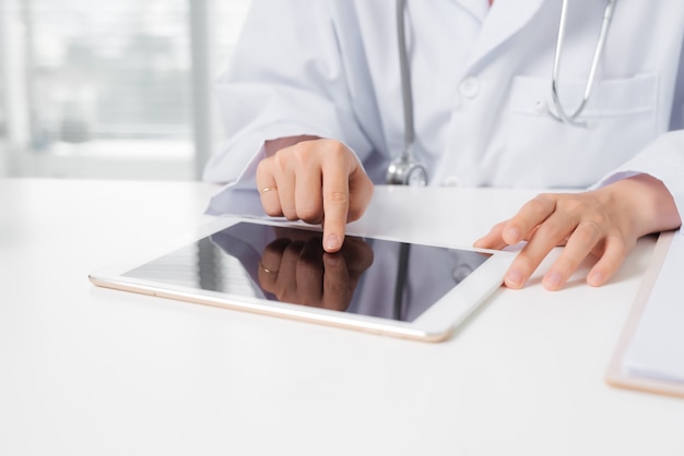 Female doctor hand touching a digital tablet while sitting at desk.