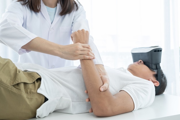 Female doctor hands doing physical therapy By extending the arm of a male patient with VR box