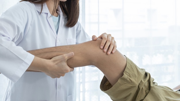 Female doctor hands doing physical therapy By extending the leg and knee of a male patient.