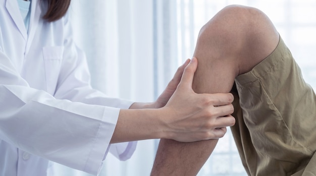 Female doctor hands doing physical therapy By extending the leg and knee of a male patient.