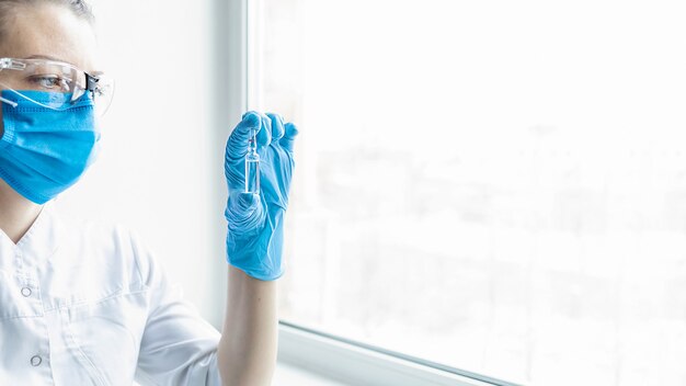 Female doctor holding ampoule with COVID-19 coronavirus vaccine in laboratory.