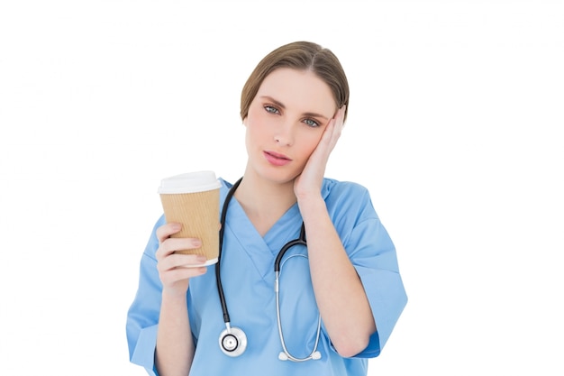 Female doctor holding a coffee mug and lifting her hand to her face