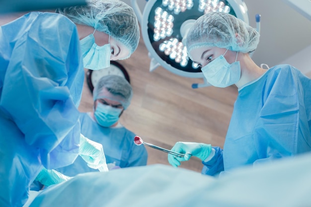 Female doctor holding cotton wool piece in forceps while two surgeons performing difficult operation