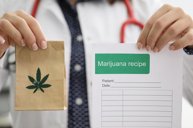 Female doctor holding marijuana recipe in one hand and package
with hemp in another