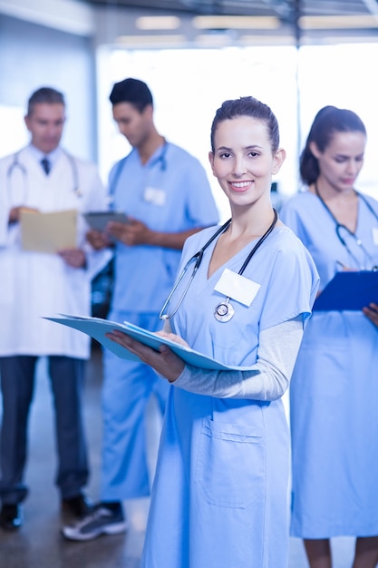 Foto medico femminile che tiene perizia medica e che sorride mentre i suoi colleghi che stanno