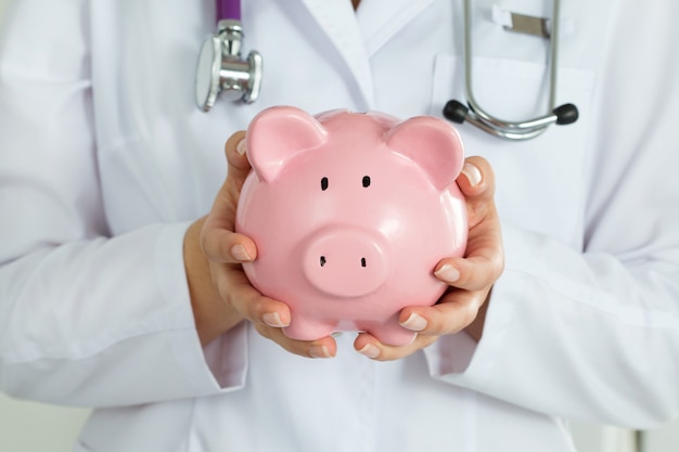 Female doctor holding a piggy bank closeup