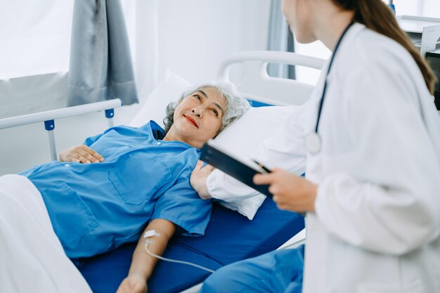 Female doctor holding senior male patient hand on the bed with receiving saline solution in hospital or clinic