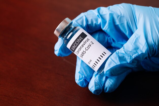 Female doctor holding syringe and COVID-19 vaccine isolated on wood background. Healthcare And Medical concept.