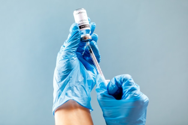 Female doctor holding syringe and COVID vaccine isolated on blue