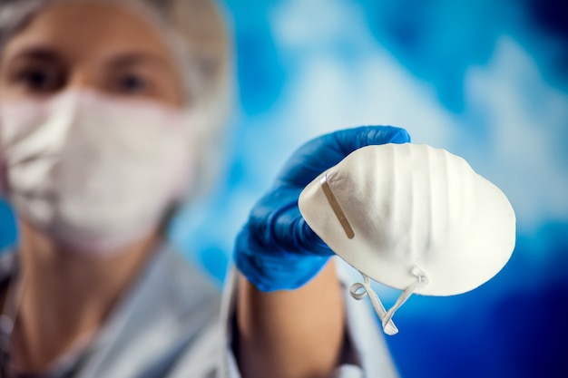 A female doctor holds medical mask in hand and shows it at camera. Medicine and healthcare concept.