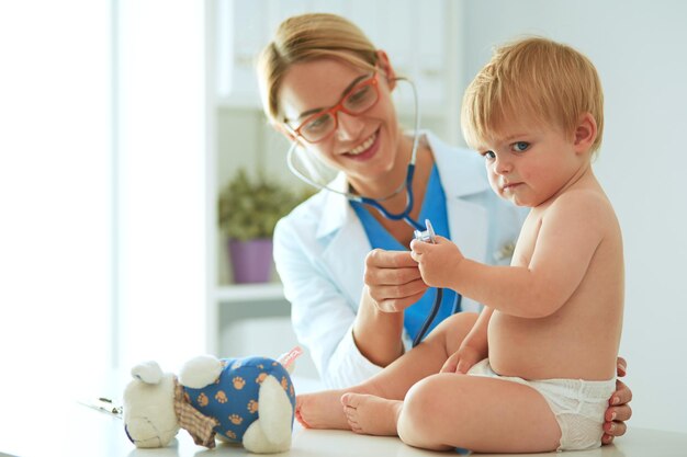 Female doctor is listening kid with a stethoscope in clinic