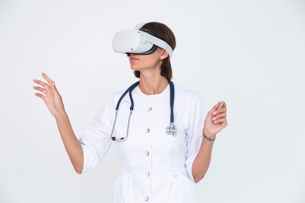 Female doctor in lab coat on white  isolated, wearing virtual reality glasses touch air