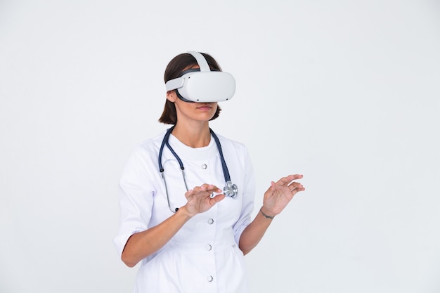 Female doctor in lab coat on white  isolated, wearing virtual reality glasses touch air