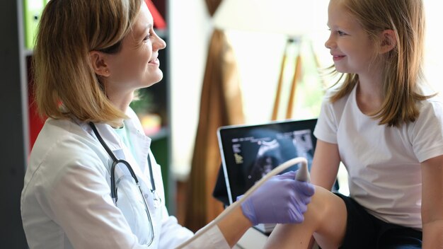 Female doctor makes ultrasound of knee of young patient in clinic girl and therapist smile at