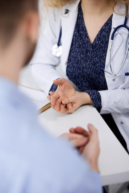 Female doctor and male patient discussing current health examination while sitting in clinic, close-up.