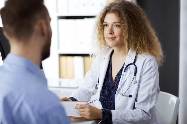 Female doctor and male patient discussing current health examination while sitting in clinic. Perfect medical service and medicine concept.