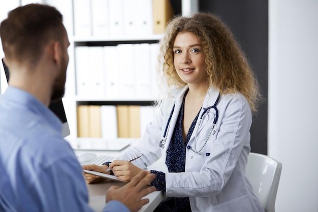 Female doctor and male patient discussing current health examination while sitting in clinic. Perfect medical service and medicine concept.