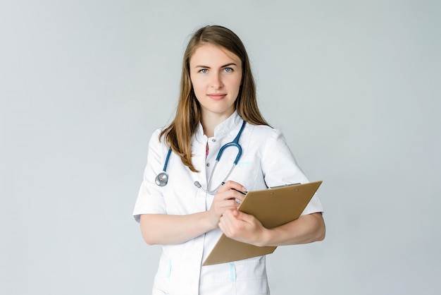 Female doctor in a mask and blue phonendoscope writes something in a folder