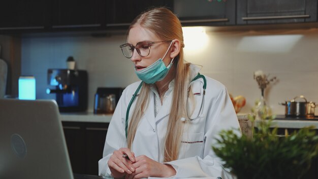 Female doctor in medical gown making video call to patient from home