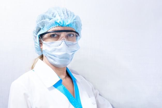 Female doctor in medical mask, hat and goggles, medical worker on a light background