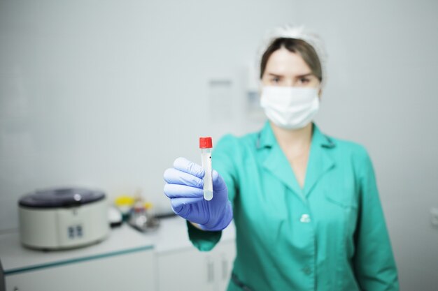 Female doctor in medical mask holding a test tube for blood test