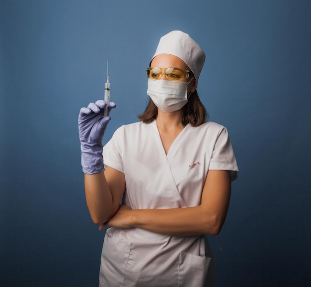 의료용 마스크를 쓴 여성 의사가 손에 주사기를 들고 있습니다. 예방 접종 개념입니다.