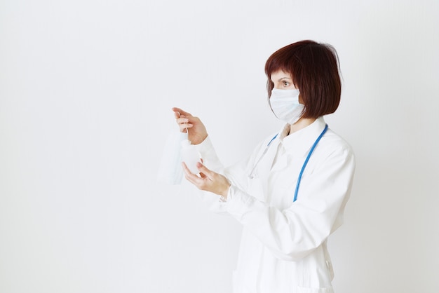 Female doctor in medical mask and uniform offers mask and disinfectant in bottle