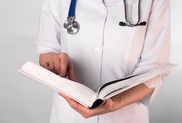 여성 의사 또는 의학에 두꺼운 책을 읽고 제복을 입은 의료 학생, 시험을 준비합니다.