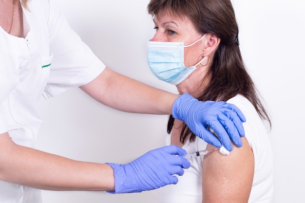 Female doctor or nurse giving shot or vaccine to patients shoulder closeup vaccination against flu v...