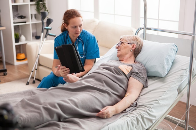 Female doctor in nursing home using tablet computer to show old woman medical results.