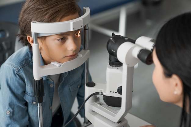 Female doctor ophthalmologist doing basic eye examination of cute boy in modern clinic