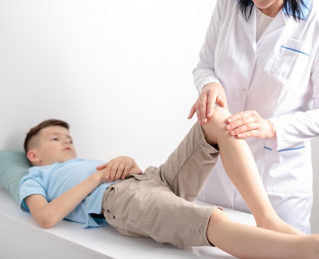 Female doctor orthopedist examines young boys knee at the hospital or clinic Trauma or pain