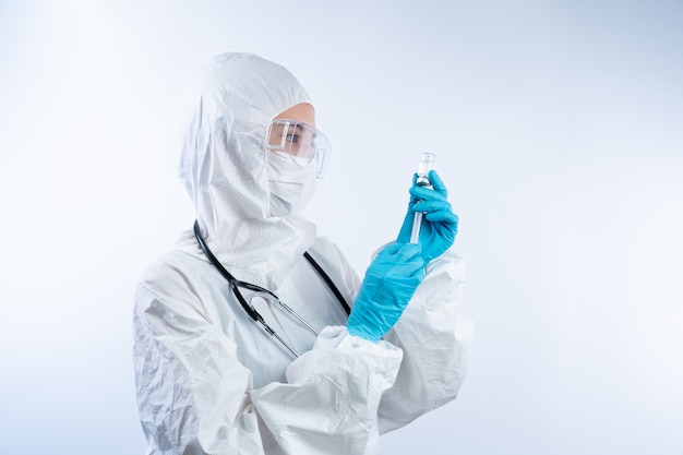 Female doctor in PPE (personal protective equipment), gloves face mask and safety glasses holding coronavirus vaccine bottle and needle.