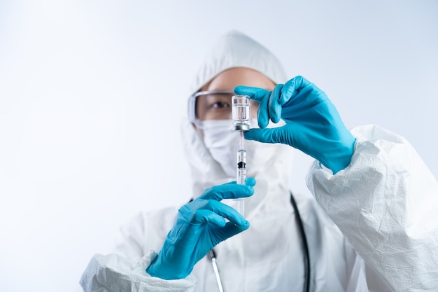 Female doctor in PPE (personal protective equipment), gloves face mask and safety glasses holding coronavirus vaccine bottle and needle.