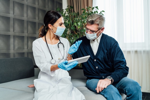 Female doctor in protective mask advises senior man visiting
home. family doctor, self-isolation.