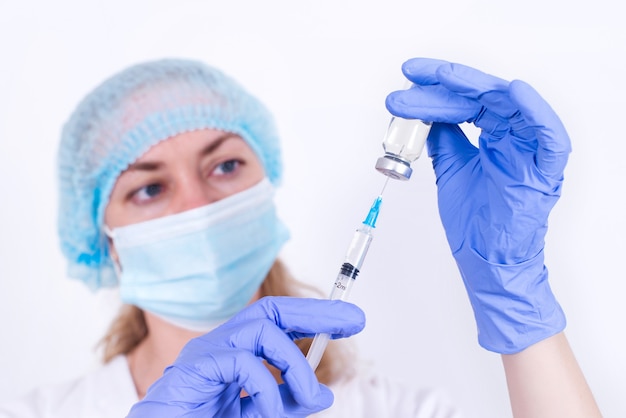 보호 마스크와 장갑을 끼고 있는 여성 의사가 주사기 근접 촬영 바이러스학자에 백신을 입력하고 있습니다