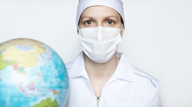 Female doctor in protective medical mask with a globe on a white background.