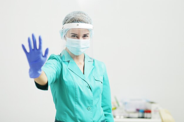 Female doctor in protective uniform shows stop gesture with hand