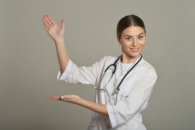Женщина-врач показывает пустую копию пространства на сером фоне