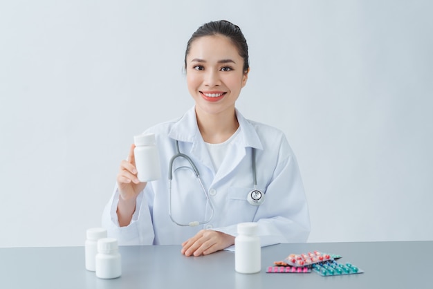 Female doctor sitting at desk, holding bottle with white pills
